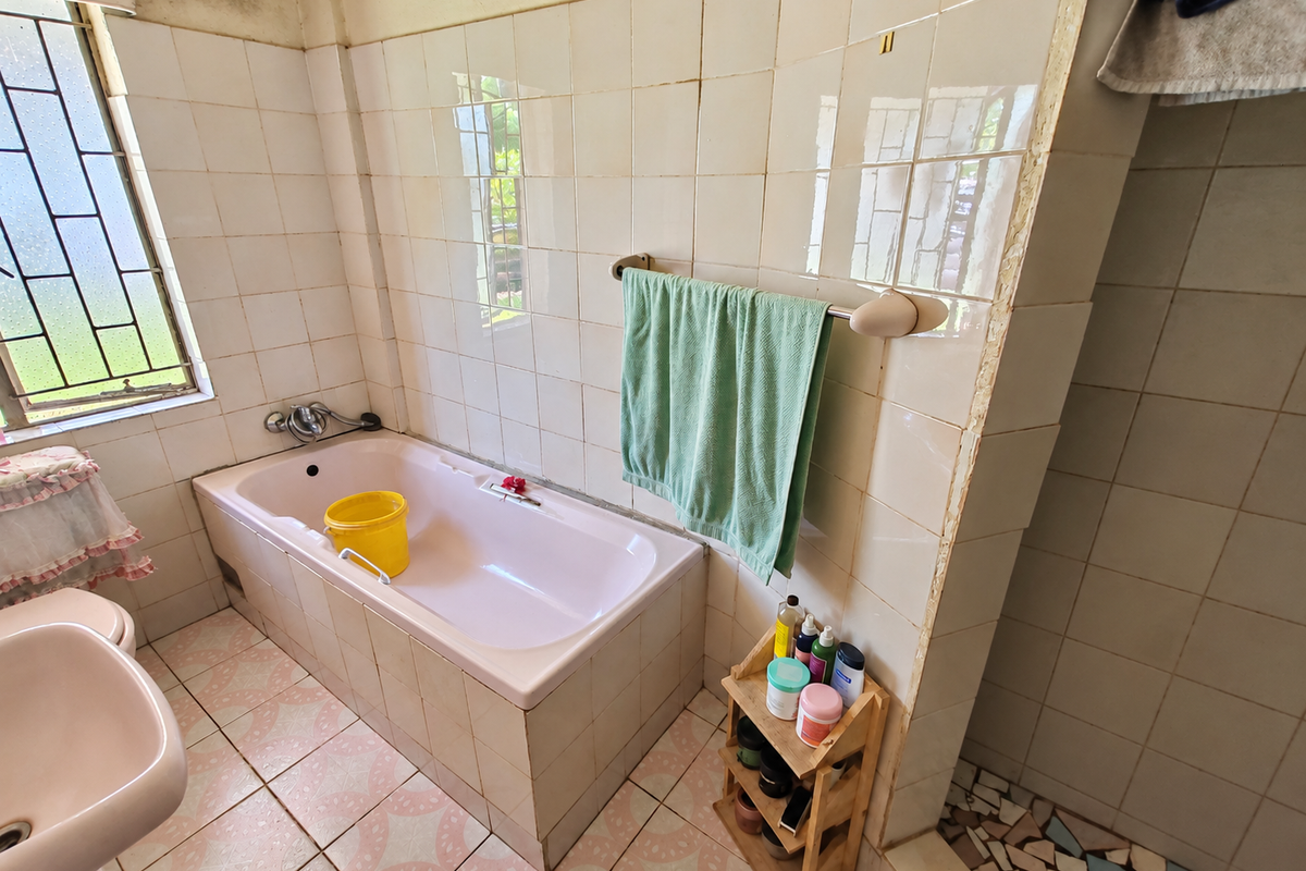 A dated bathroom featuring a built-in bathtub, pedestal basin, and original ceramic tiling, requiring modernization and repair of wall finishes.