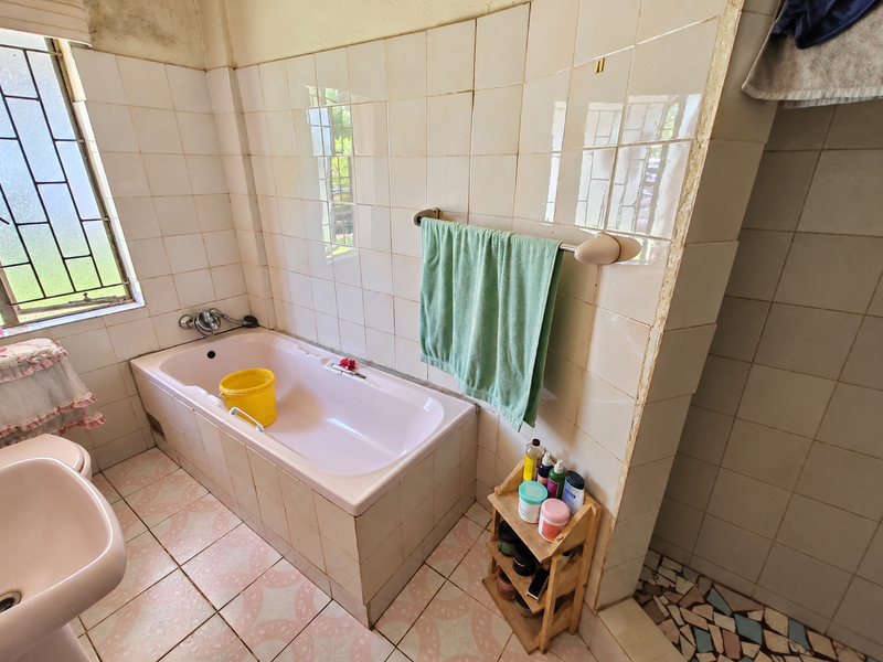 A dated bathroom featuring a built-in bathtub, pedestal basin, and original ceramic tiling, requiring modernization and repair of wall finishes.