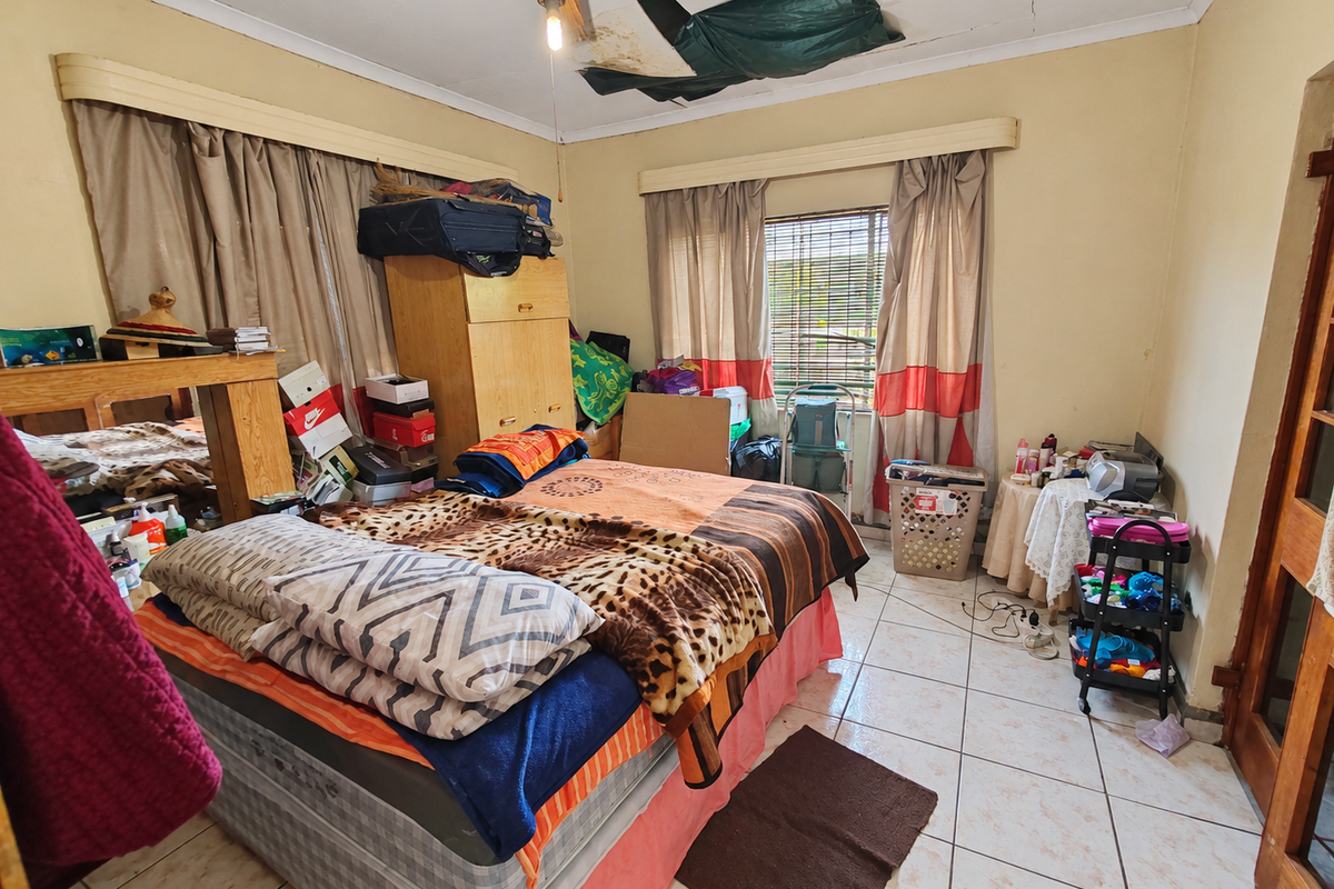 A bedroom featuring tiled flooring and a ceiling fan, currently requiring ceiling repairs and general maintenance to improve the living space.