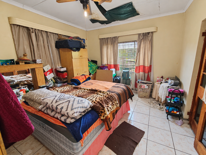 A bedroom featuring tiled flooring and a ceiling fan, currently requiring ceiling repairs and general maintenance to improve the living space.