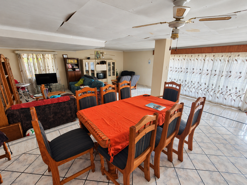 Spacious open-plan living and dining area featuring tiled flooring, a ceiling fan, and large sliding doors, requiring ceiling repairs.