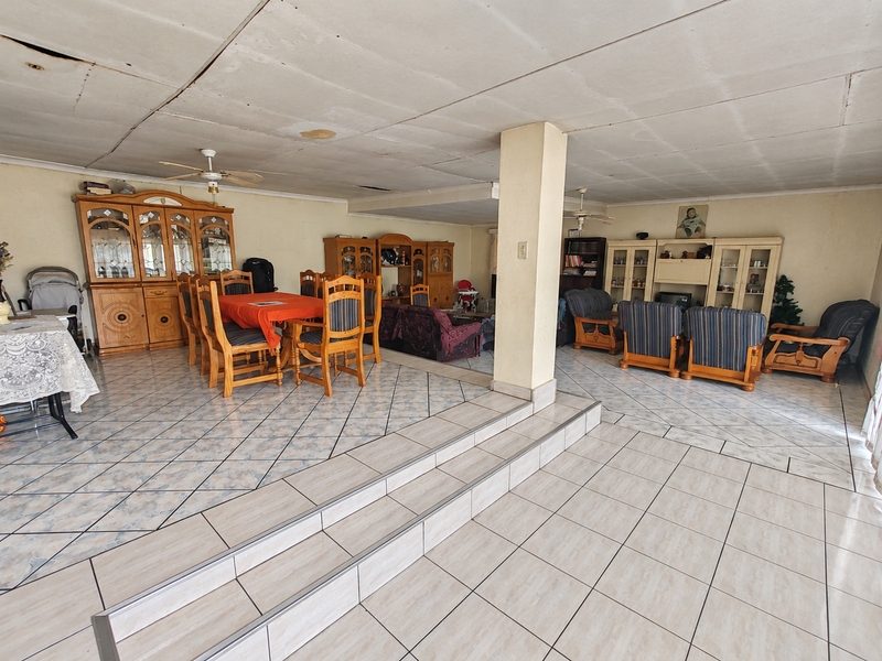 Spacious open-plan living and dining area featuring split-level tiled flooring, ceiling fans, and a central structural column, offering significant potential for modernization.