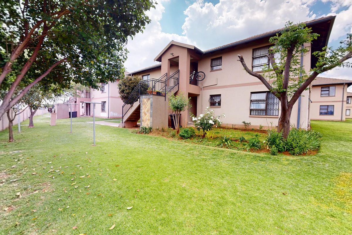 Rear view of a multi-story apartment complex featuring a communal lawn, landscaped garden areas, and external staircase access to upper units.