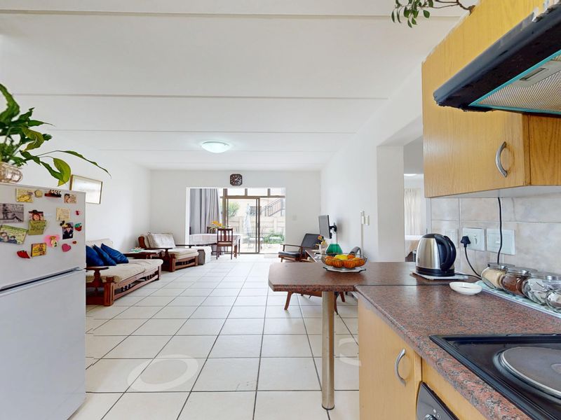 Open-plan living area featuring a functional kitchen with built-in cabinetry and tiled flooring, leading through to a bright lounge with sliding door access.