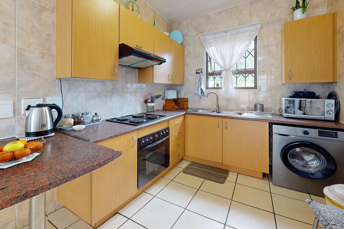 A functional kitchen featuring laminate cabinetry, granite-look countertops, built-in oven with hob, extractor fan, and tiled finishes throughout.