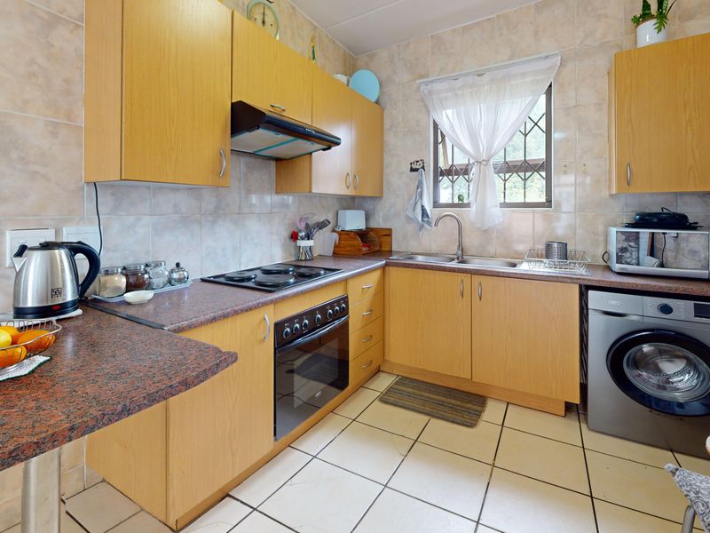 A functional kitchen featuring laminate cabinetry, granite-look countertops, built-in oven with hob, extractor fan, and tiled finishes throughout.