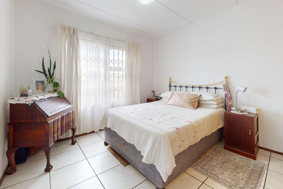 A well-lit bedroom featuring tiled flooring, a window with security bars, and built-in wardrobe storage.