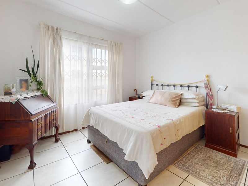 A well-lit bedroom featuring tiled flooring, a window with security bars, and built-in wardrobe storage.
