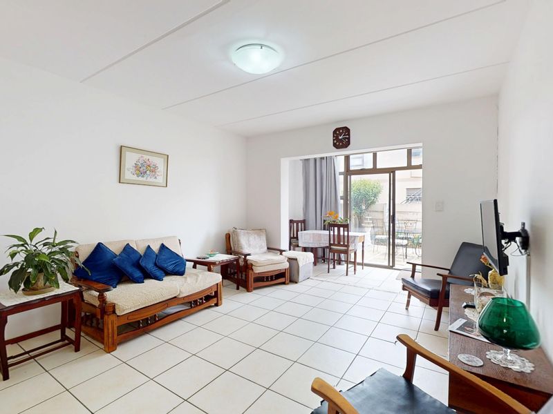 A bright living room featuring neutral tiled flooring and a sliding glass door providing access to an outdoor patio area.