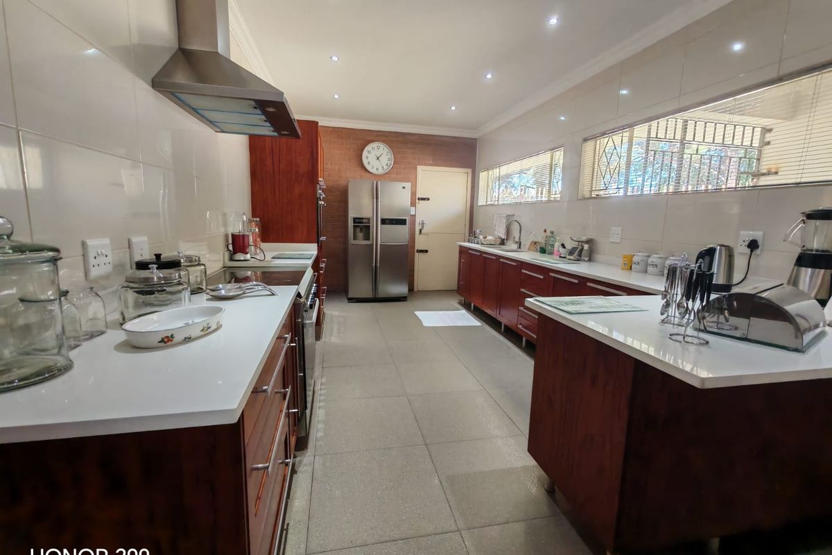 Spacious kitchen featuring dark wood cabinetry, white stone countertops, stainless steel extractor fan, and a distinctive exposed brick wall with tiled flooring.