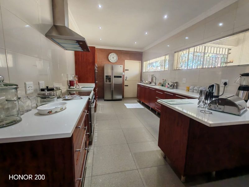 Spacious kitchen featuring dark wood cabinetry, white stone countertops, stainless steel extractor fan, and a distinctive exposed brick wall with tiled flooring.