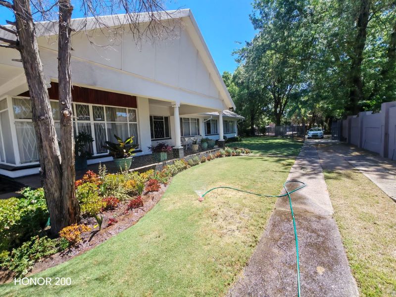 Front elevation of a house featuring a covered veranda, leaded glass windows, and a landscaped garden with a concrete driveway.