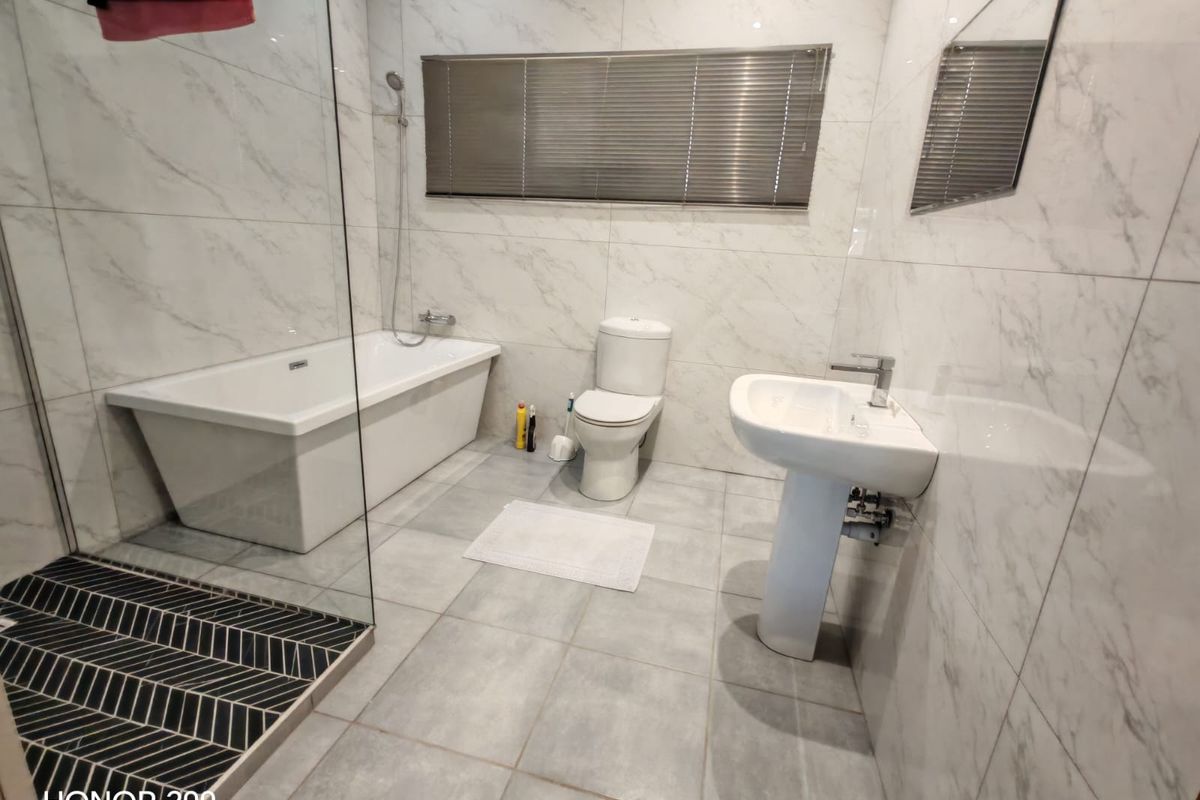 Modern bathroom featuring a freestanding bathtub, separate shower with glass screen, pedestal basin, and marble-look wall tiling.