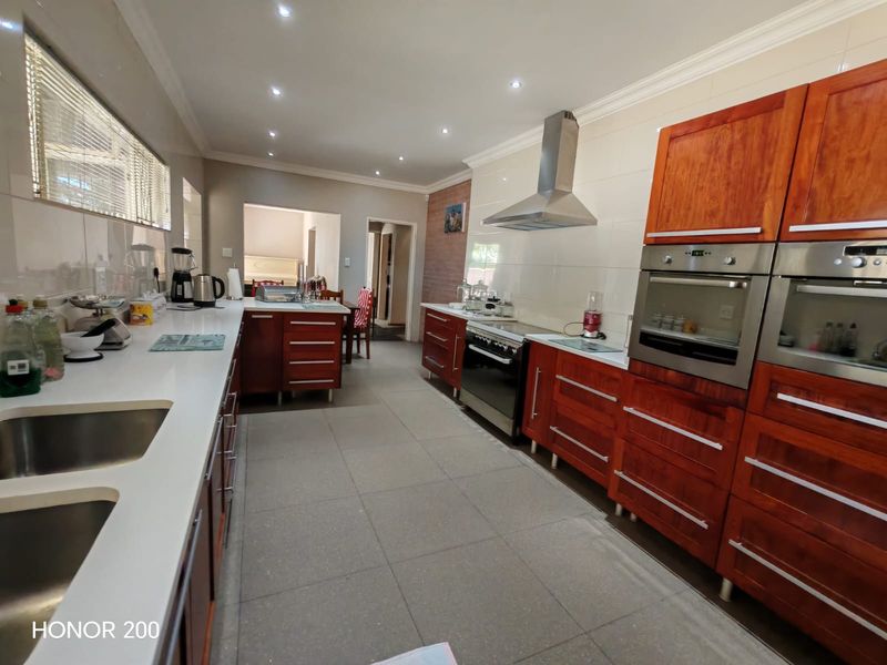 Spacious kitchen featuring warm-toned wooden cabinetry, stone countertops, integrated stainless steel appliances, and modern recessed lighting with a functional tiled layout.