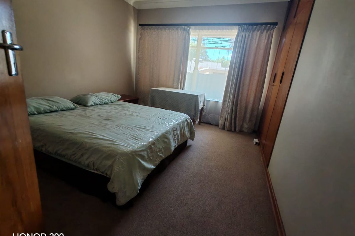 A standard bedroom featuring built-in wooden wardrobes, carpeted flooring, and a window with curtains.