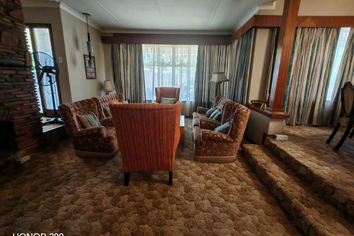 Spacious sunken living room featuring a prominent stone fireplace, timber architectural detailing, and large windows, offering a classic layout with significant renovation potential.