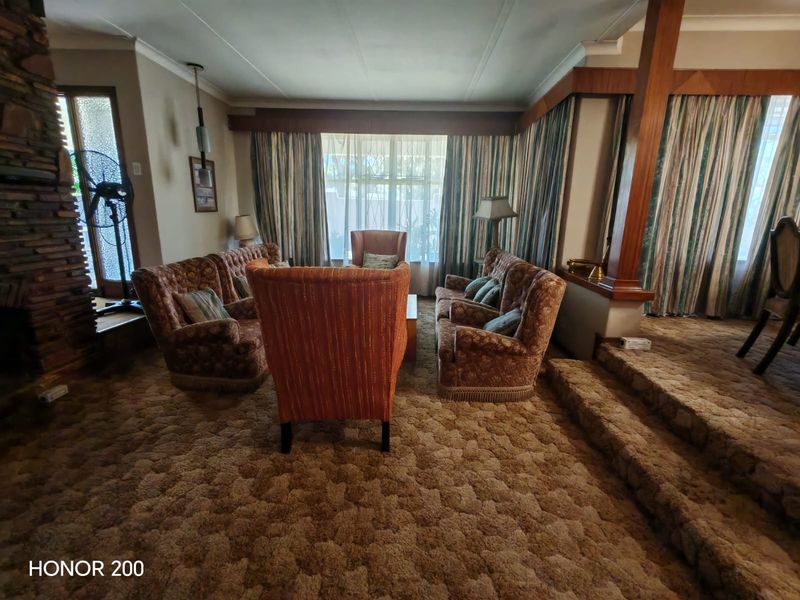 Spacious sunken living room featuring a prominent stone fireplace, timber architectural detailing, and large windows, offering a classic layout with significant renovation potential.