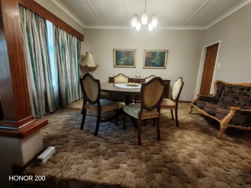 A traditional dining room featuring coved ceilings, carpeted flooring, and a fitted curtain pelmet, offering a dated aesthetic ready for modernization.