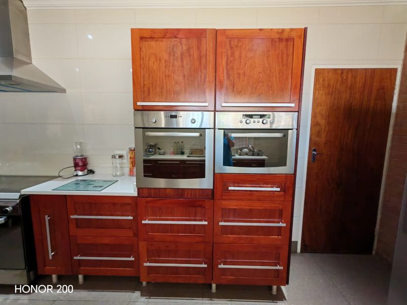 A kitchen featuring warm-toned wooden cabinetry, integrated stainless steel ovens, a built-in microwave, and a tiled splashback.