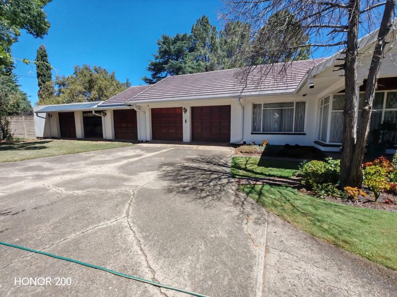 Front elevation of a residential property featuring a triple garage, tiled roof, and a spacious concrete driveway set within a landscaped garden.