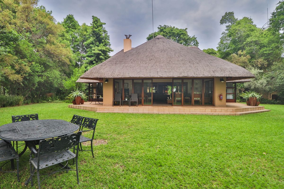 Rear view of a house featuring a traditional thatch roof, a spacious tiled patio, and large sliding glass doors opening onto a lush garden.