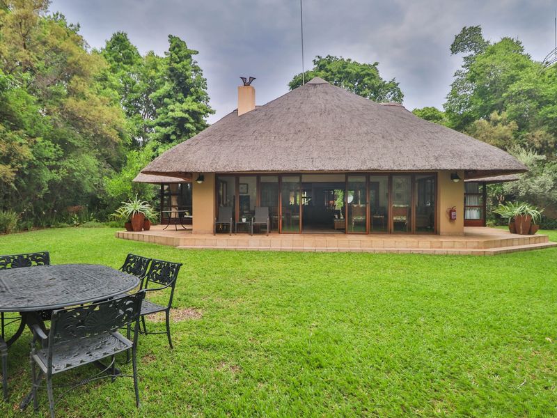 Rear view of a house featuring a traditional thatch roof, a spacious tiled patio, and large sliding glass doors opening onto a lush garden.