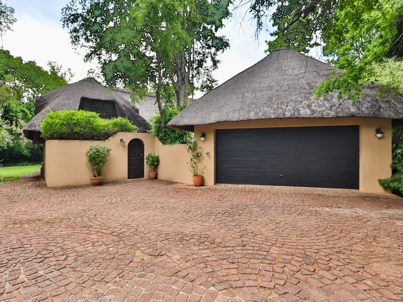 Front exterior view featuring a double garage with a thatched roof, a cobblestone driveway, and a secure arched pedestrian entrance.