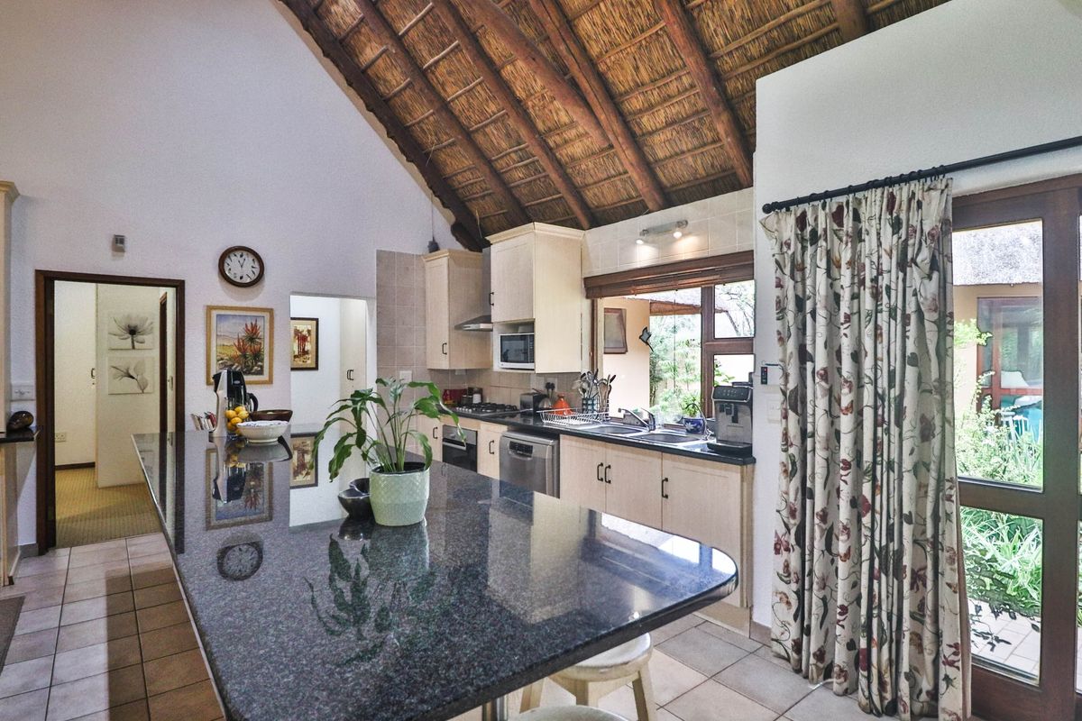 A spacious kitchen featuring a large granite island, built-in cabinetry, and a distinctive vaulted thatched ceiling with direct access to the outdoor area.