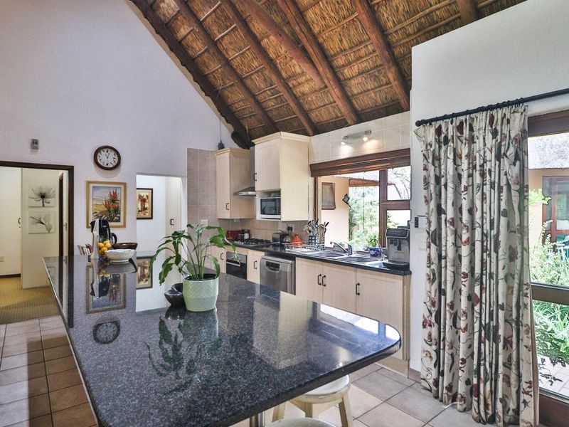 A spacious kitchen featuring a large granite island, built-in cabinetry, and a distinctive vaulted thatched ceiling with direct access to the outdoor area.