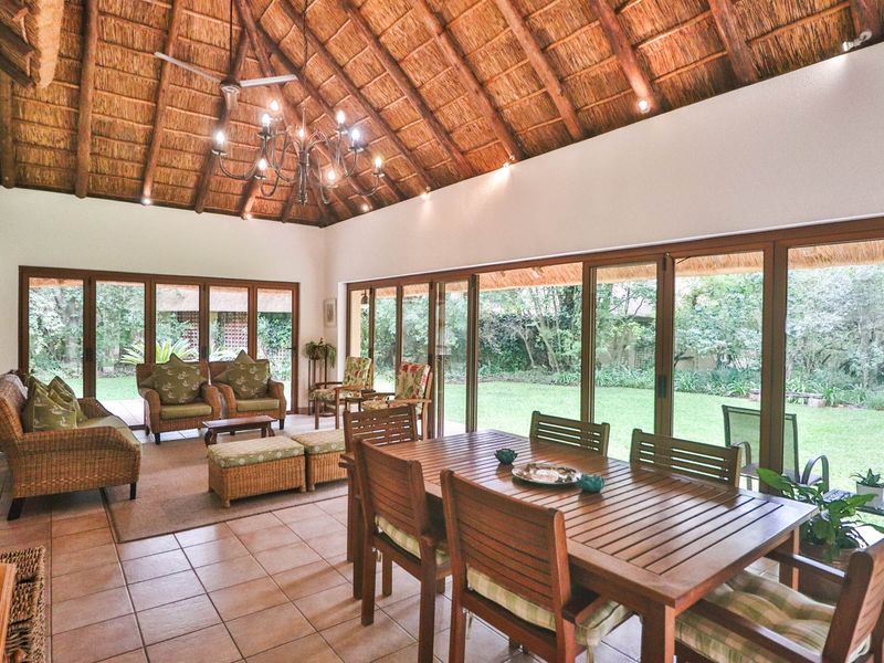 Spacious open-plan living and dining area featuring a high vaulted thatched ceiling with exposed rafters, ceramic tiling, and expansive sliding doors opening to the garden.
