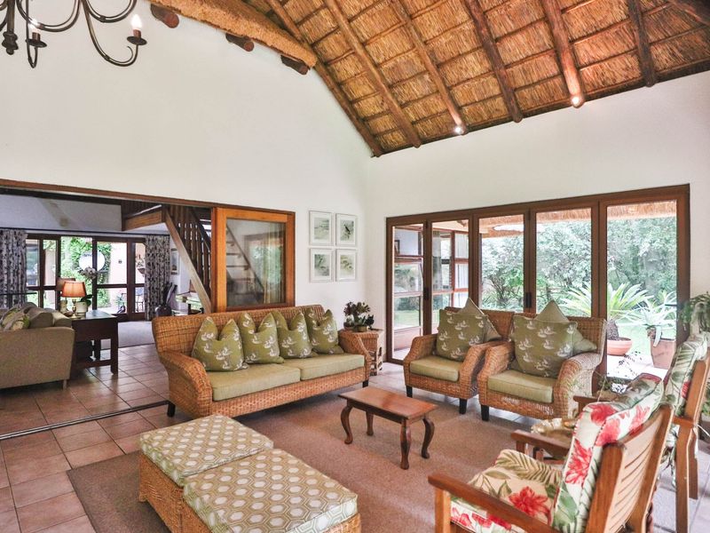 Spacious living room featuring a high vaulted thatched ceiling with exposed timber rafters, tiled flooring, and large timber-framed sliding doors opening to the garden.