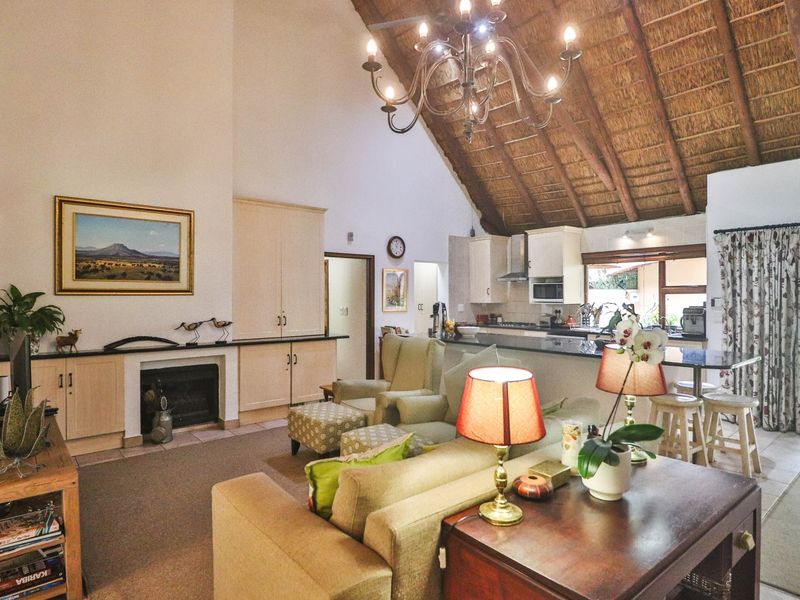 Spacious open-plan living area featuring a high vaulted thatched ceiling with exposed rafters, a built-in fireplace, and a functional kitchen with a breakfast island.