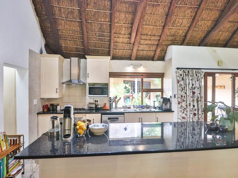 A charming kitchen featuring a large granite island, built-in cabinetry, and a unique exposed thatched roof ceiling, creating a warm and rustic atmosphere.