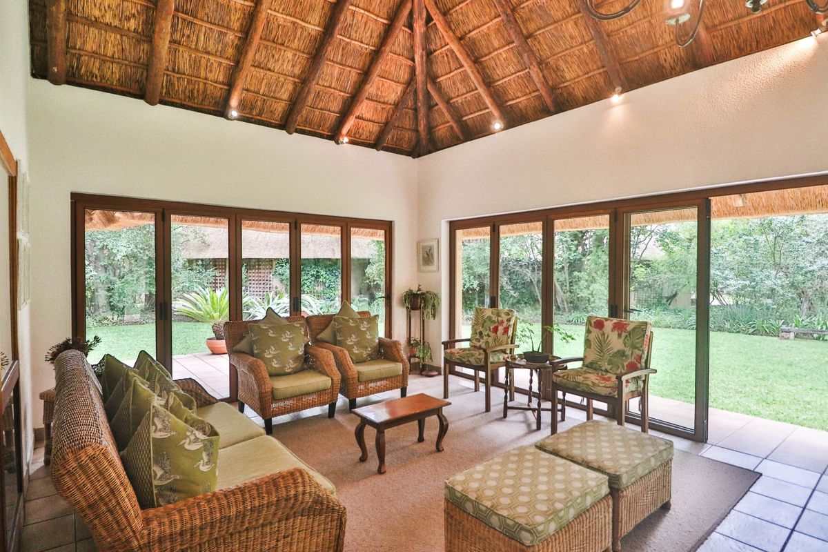 Spacious living room featuring a high vaulted thatched ceiling with exposed timber rafters and large sliding glass doors opening onto the garden.