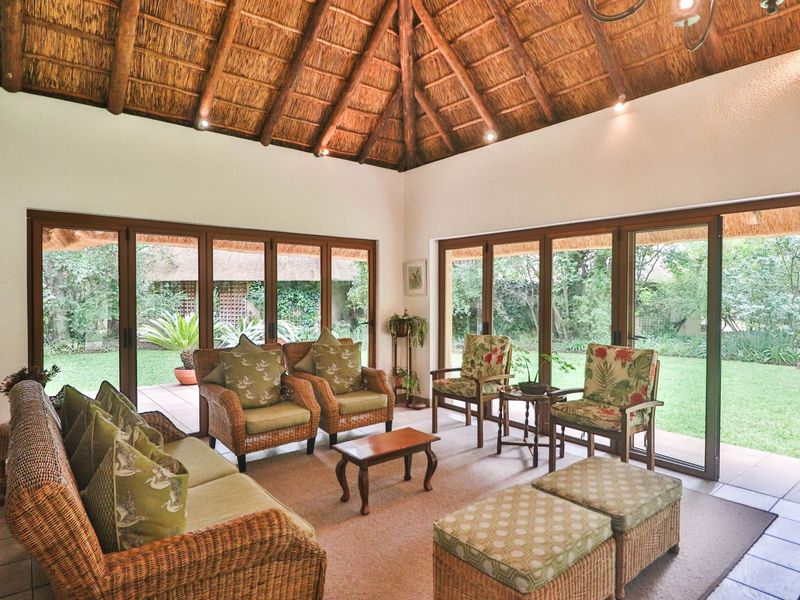 Spacious living room featuring a high vaulted thatched ceiling with exposed timber rafters and large sliding glass doors opening onto the garden.