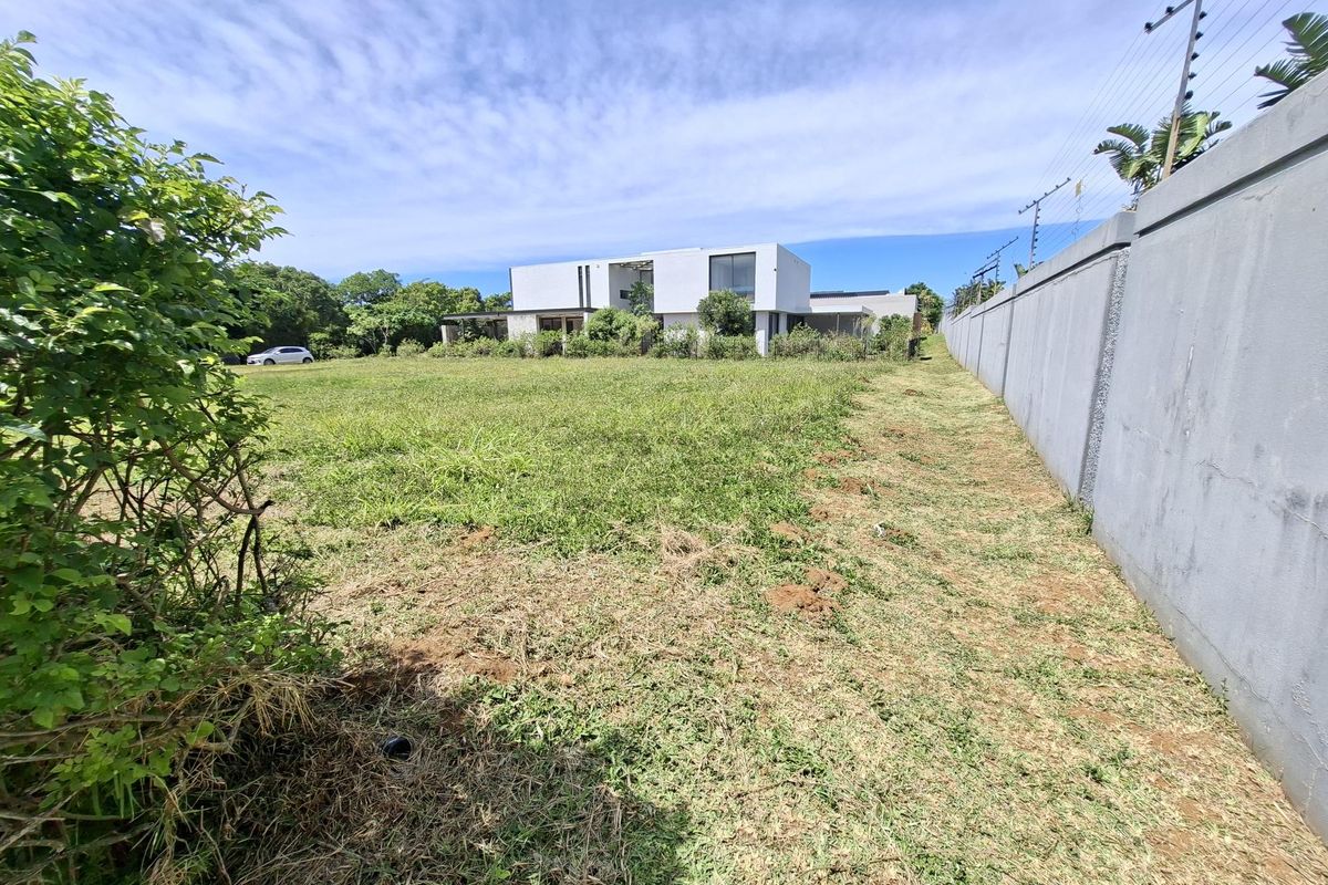 A view of a vacant residential plot featuring a perimeter wall with electric fencing, looking towards a modern neighboring property.