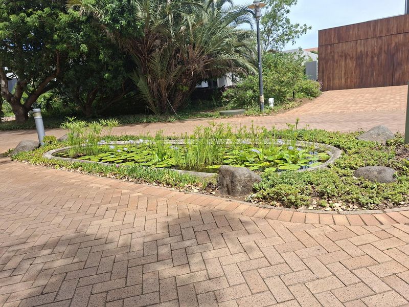 A well-maintained landscaped garden area featuring a central ornamental pond surrounded by brick paving and mature trees.
