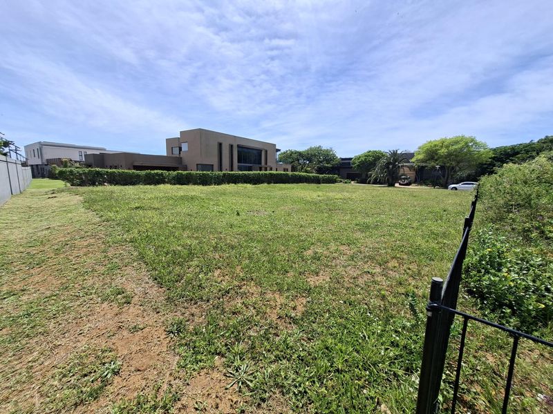 A spacious, level residential vacant plot featuring established perimeter fencing and a well-maintained hedge, offering a clear site for future development.