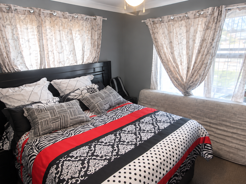 A bedroom featuring grey walls, carpeted flooring, and a built-in wardrobe, offering a functional space with natural light from the windows.
