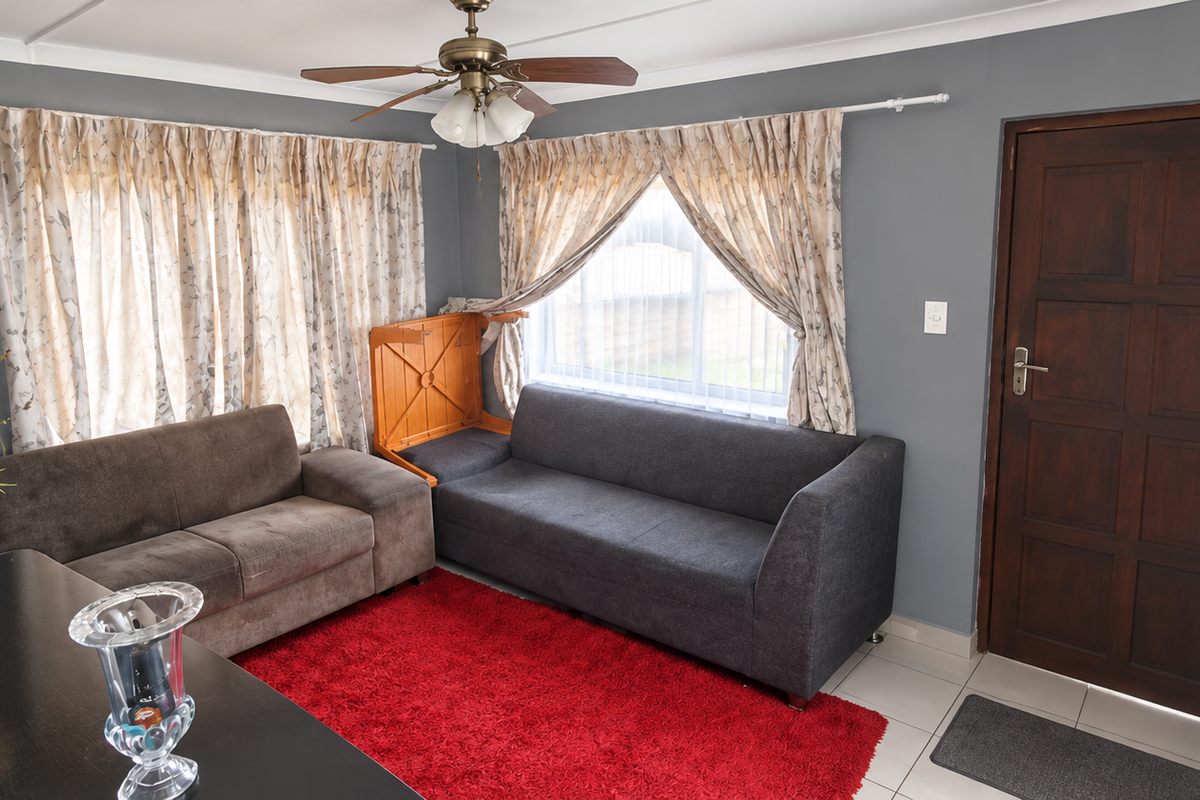 A living room featuring tiled flooring, a ceiling fan, and a solid timber entrance door with natural light from multiple windows.
