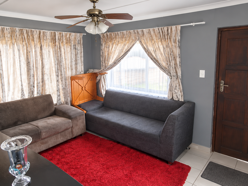 A living room featuring tiled flooring, a ceiling fan, and a solid timber entrance door with natural light from multiple windows.