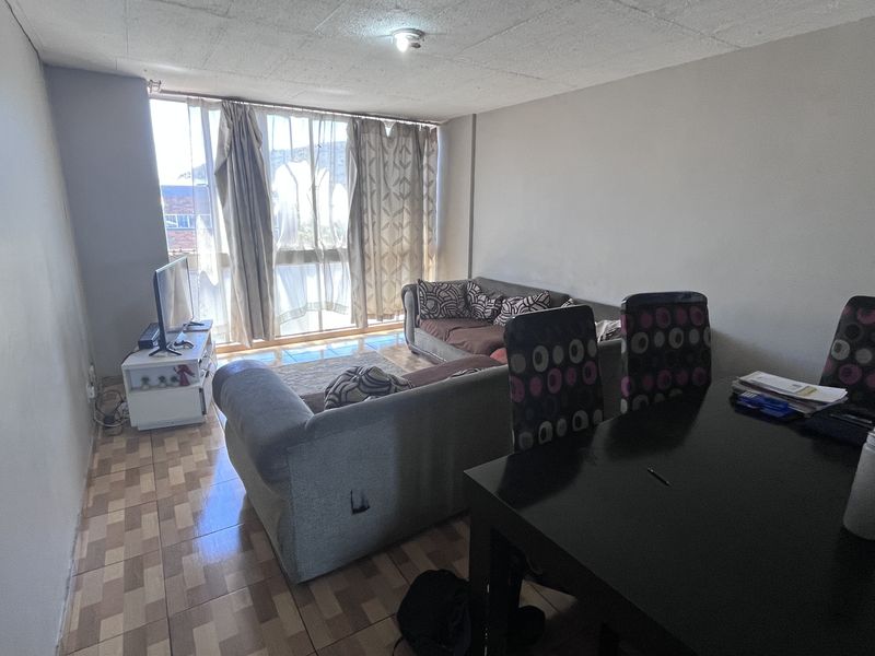 Open plan living and dining area featuring tiled flooring and a large window providing natural light, in need of cosmetic updates.