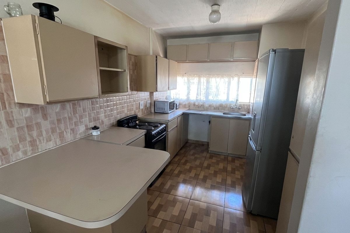 A functional kitchen featuring laminate countertops, tiled backsplash, built-in cabinetry, and a stainless steel sink, offering potential for modern updates.