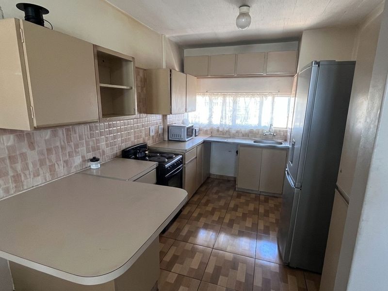 A functional kitchen featuring laminate countertops, tiled backsplash, built-in cabinetry, and a stainless steel sink, offering potential for modern updates.