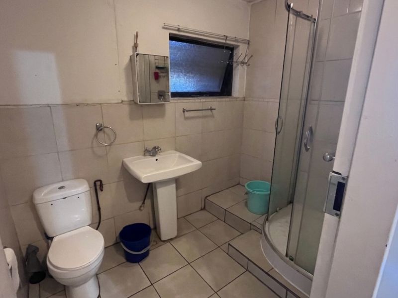 A functional bathroom featuring a pedestal basin, toilet, and a glass-enclosed shower with tiled finishes throughout.