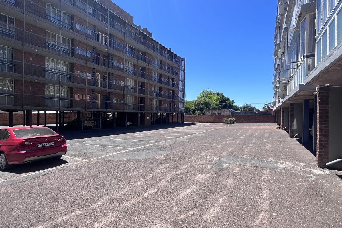An exterior view of the townhouse complex showing the paved parking area between the multi-story residential buildings.