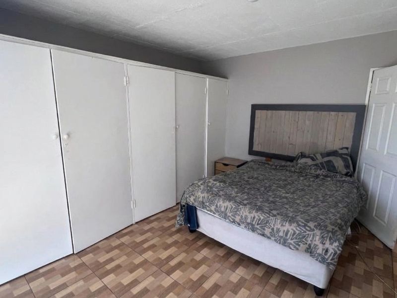 A bedroom featuring built-in cupboards, tiled flooring, and a standard panel door, offering a functional space with potential for cosmetic updates.