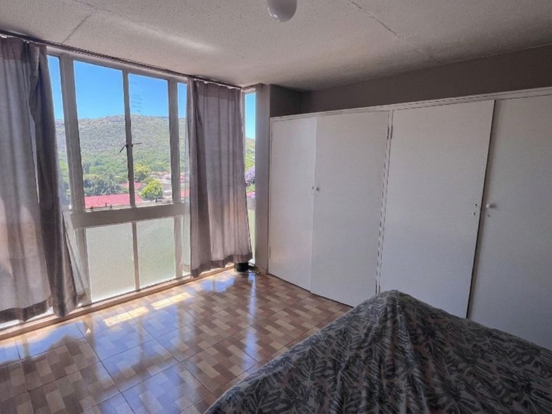 A bedroom featuring built-in cupboards, tiled flooring, and large windows offering natural light and scenic views.