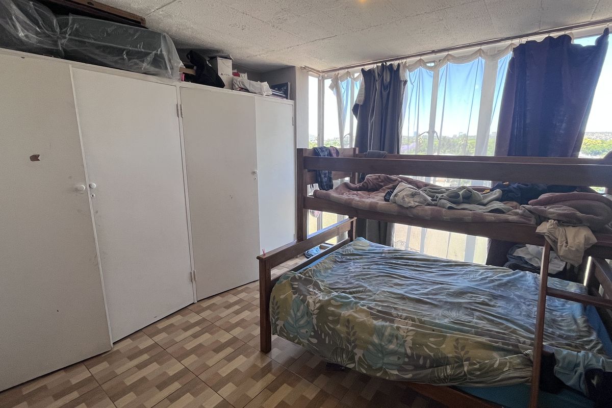 A bedroom featuring built-in cupboards, tiled flooring, and a large window providing natural light.