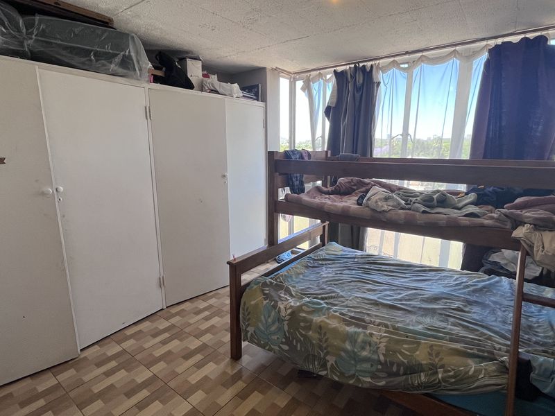 A bedroom featuring built-in cupboards, tiled flooring, and a large window providing natural light.